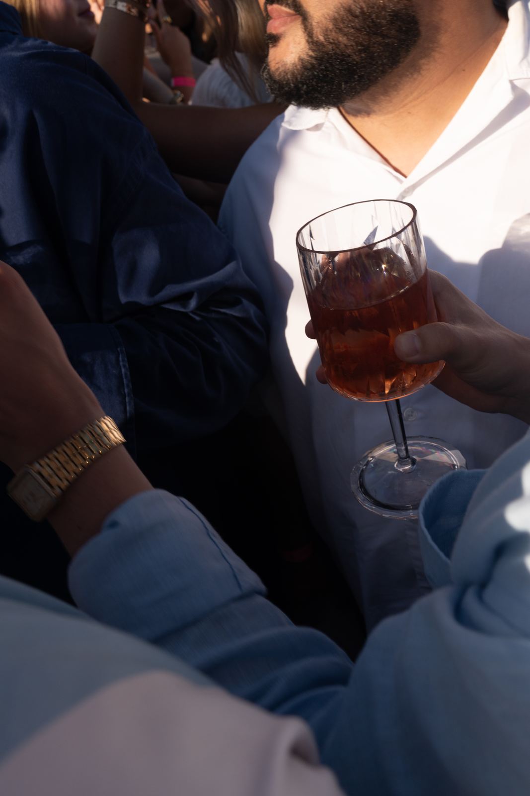 Hand hält ein Glas HEAVEN Rosé im warmen Abendlicht, daneben ein Arm mit goldener Uhr